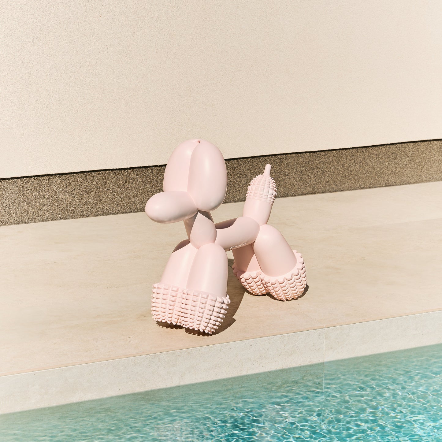 Pink Sanddog balloon dog chew toy on a striped background with water at the bottom
