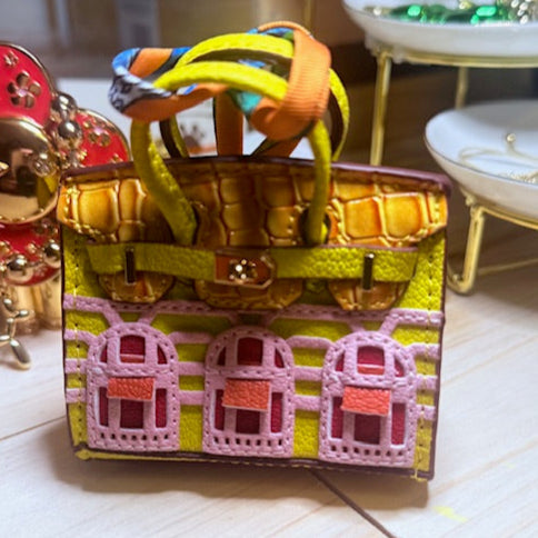 A leather mini purse dog waste bag dispenser in the colors pink, green, and gold, designed to look like a small handbag.