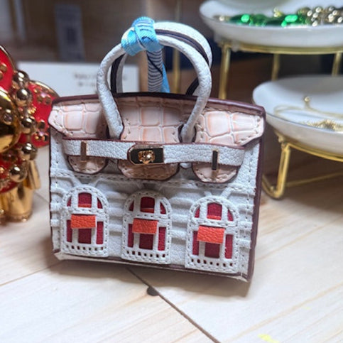 A leather mini purse dog waste bag dispenser in the colors pink, green, and gold, designed to look like a small handbag.