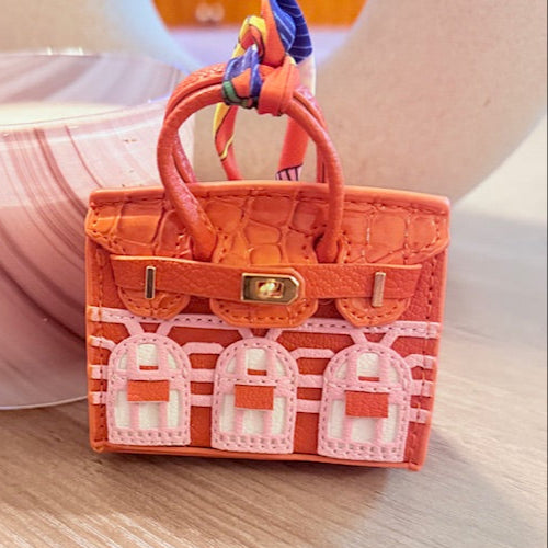 A leather mini purse dog waste bag dispenser in the colors pink, green, and gold, designed to look like a small handbag.