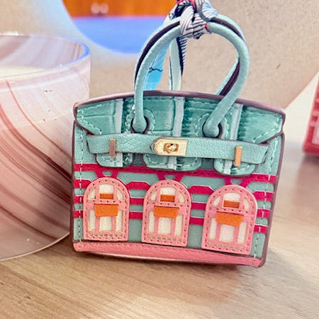 A leather mini purse dog waste bag dispenser in the colors pink, green, and gold, designed to look like a small handbag.