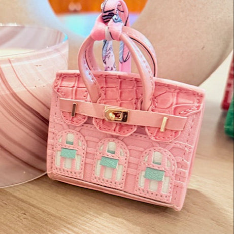 A leather mini purse dog waste bag dispenser in the colors pink, green, and gold, designed to look like a small handbag.