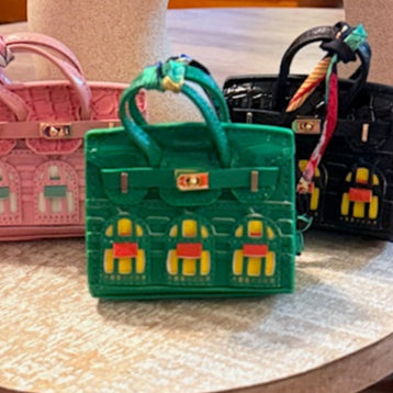 A leather mini purse dog waste bag dispenser in the colors pink, green, and gold, designed to look like a small handbag.