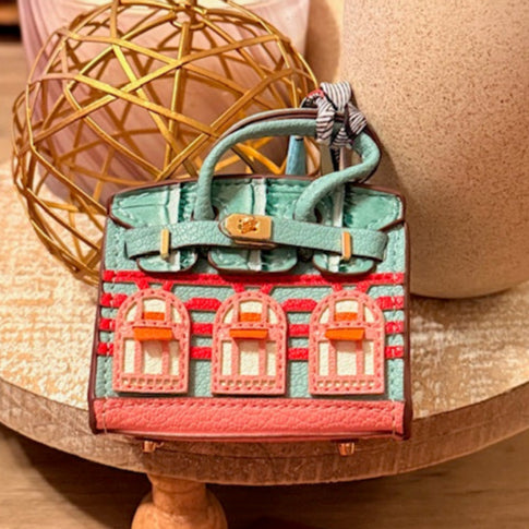 A leather mini purse dog waste bag dispenser in the colors pink, green, and gold, designed to look like a small handbag.