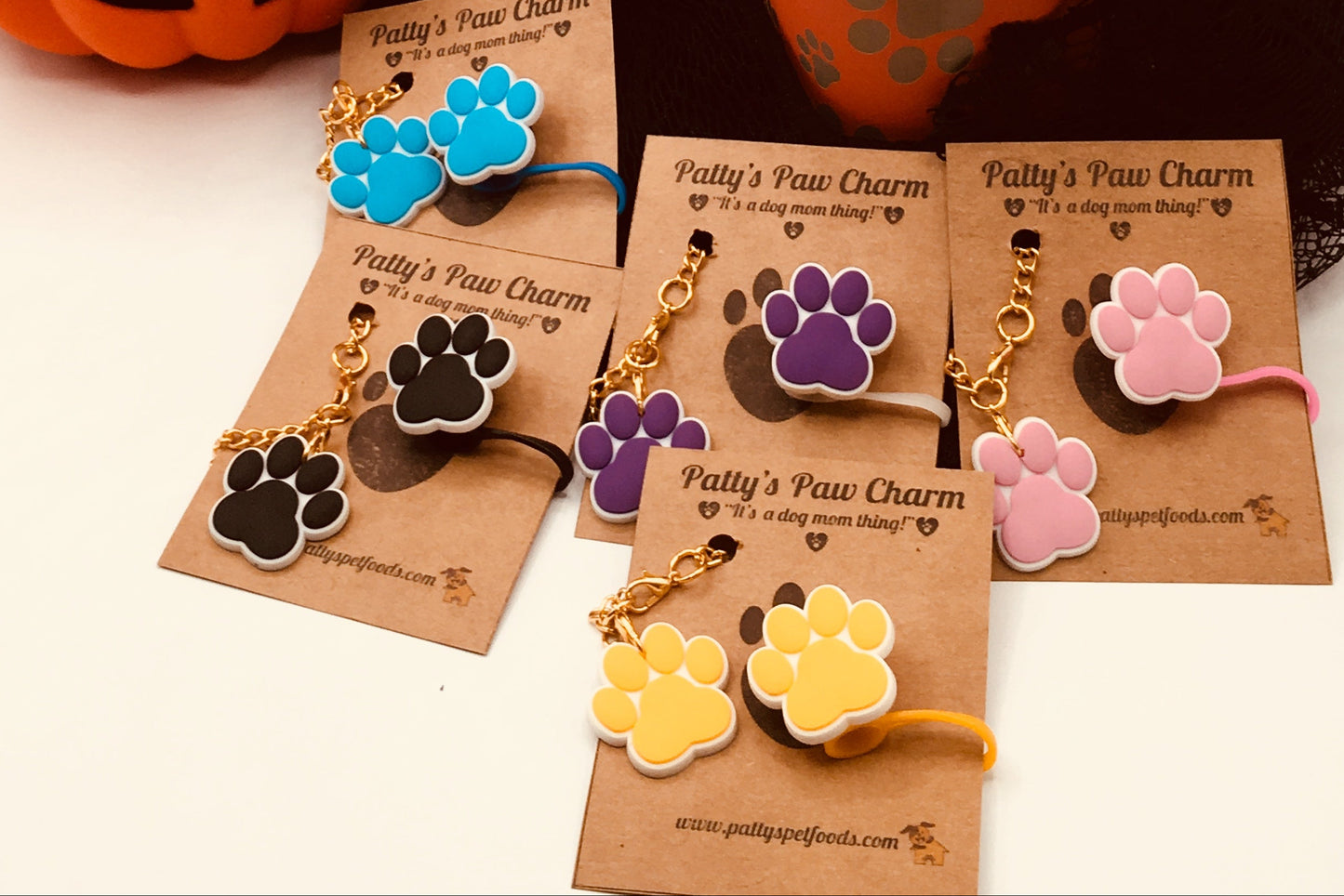 A silicone water bottle straw cap with a paw print design, displayed along with a few paw print charms, against a backdrop featuring a pumpkin and autumn decorations.