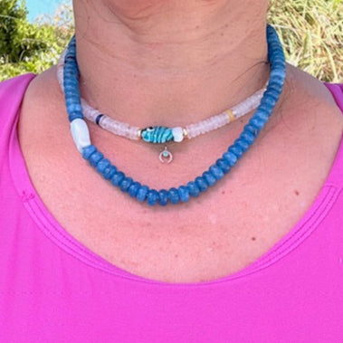 Person wearing a blue beaded necklace and pink top outdoors