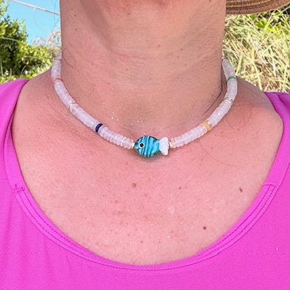 Person wearing a pink tank top and straw hat with a necklace featuring a blue and white bead.