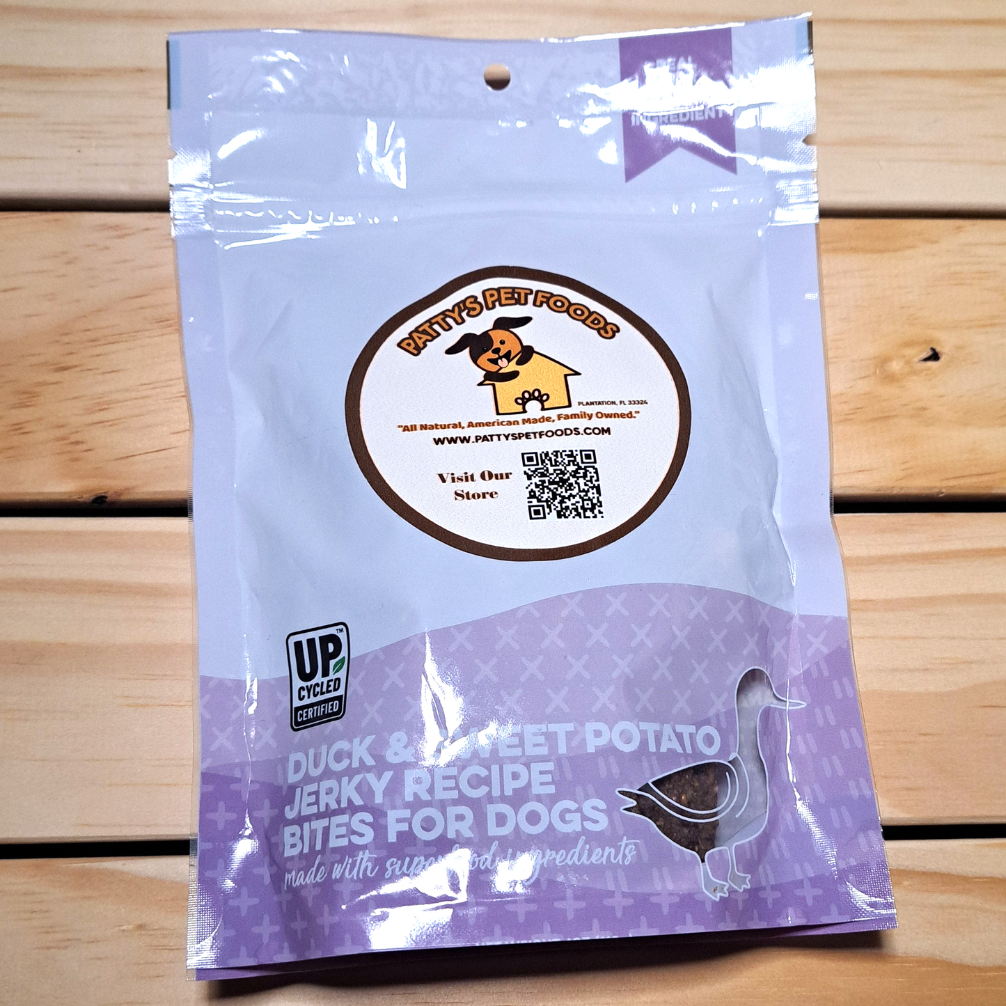 One bag of Pooch Perfect Dog Jerky Duck and Sweet Potato Treats laid on a wooden surface. The packaging is purple with images of duck and sweet potato, and product information is visible.