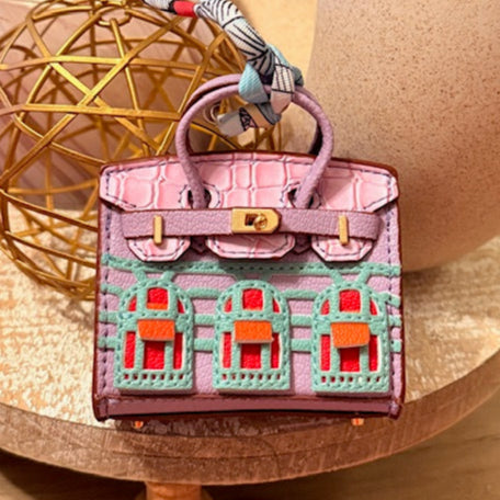 A leather mini purse dog waste bag dispenser in the colors pink, green, and gold, designed to look like a small handbag.
